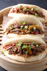 Delicious gua bao in bamboo steamer on black table, closeup