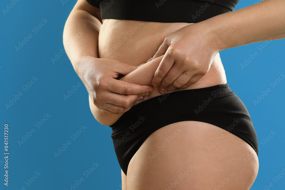 Poster Woman touching belly fat on light blue background, closeup. Overweight problem