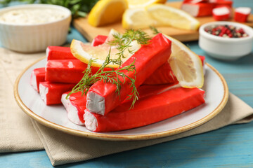 Tasty crab sticks, pieces of lemon and dill on light blue wooden table, closeup
