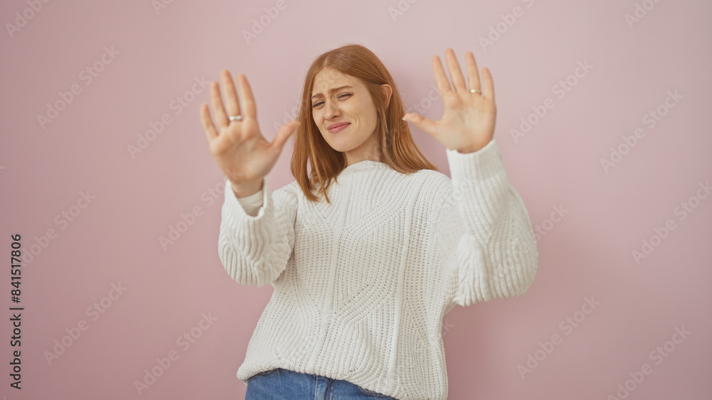 Sticker young caucasian woman in white sweater posing with hands up against a pink background, expressing st