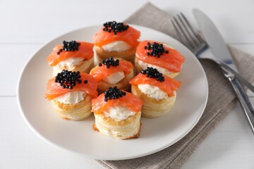 Delicious puff pastry with cream cheese, salmon, black caviar and cutlery on white wooden table