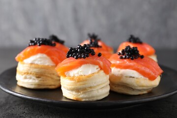 Delicious puff pastry with cream cheese, salmon and black caviar on grey table, closeup