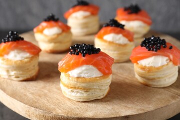 Delicious puff pastry with cream cheese, salmon and black caviar on wooden stand, closeup