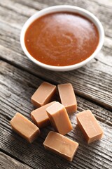 Yummy candies and caramel sauce in bowl on wooden table, closeup