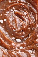 Tasty caramel sauce and salt as background, above view