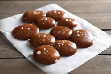 Tasty caramel candies and salt on wooden table, closeup