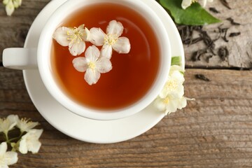 Aromatic jasmine tea in cup, flowers and dry leaves on wooden table, top view