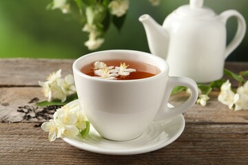 Aromatic jasmine tea in cup, flowers, dry leaves and teapot on wooden table outdoors