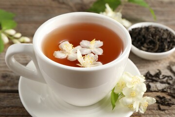 Aromatic jasmine tea in cup, flowers and dry leaves on wooden table, closeup