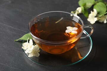 Aromatic jasmine tea in glass cup, flowers and green leaves on grey table, closeup