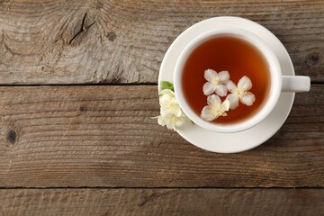 Aromatic jasmine tea in cup and flowers on wooden table, top view. Space for text