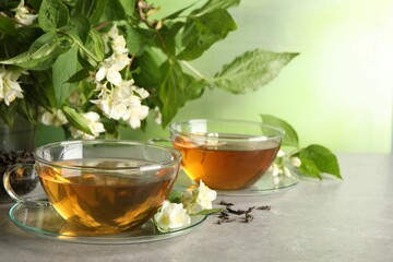 Aromatic jasmine tea in cups, flowers and green leaves on light grey table