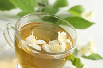 Aromatic jasmine tea in cup, flowers and green leaves on table, closeup
