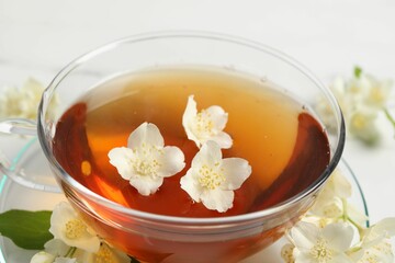 Hot jasmine tea in cup and flowers on white marble table, closeup