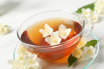 Hot jasmine tea in cup and flowers on white marble table, closeup