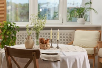 Clean dishware, flowers, fresh pastries and burning candles on table in stylish dining room