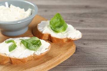 Delicious sandwiches with cream cheese and basil leaves on wooden table, closeup