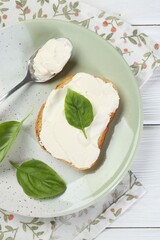 Delicious sandwich with cream cheese and basil leaves on white wooden table, top view