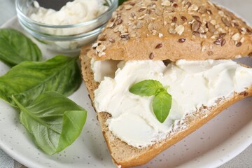 Pieces of bread with cream cheese and basil leaves on plate, closeup