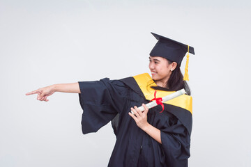 A happy female graduate of bachelor of science holding her diploma pointing to the left. Isolated...