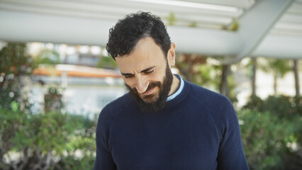 Bearded man smiling leisurely in a lush garden setting under daylight