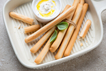 Beige serving tray with italian bread sticks grissini and ricotta dip, horizontal shot, middle close-up, selective focus