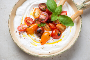 Beige serving pan with ricotta dipping sauce, roasted tomatoes and basil, horizontal shot, middle...