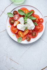 Caprese salad with buffalo mozzarella, tomatoes and fresh basil, flat lay on a white granite background, vertical shot, copy space