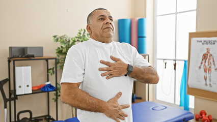 Obraz premium Middle-aged hispanic man experiencing discomfort in a well-equipped physical therapy clinic.