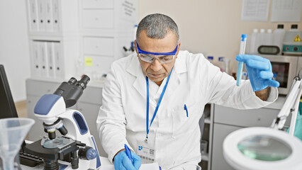 A middle-aged hispanic man in lab attire meticulously taking notes in a modern laboratory setting.