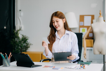 Fashion designer woman talking smart phone and using laptop with digital tablet computer in modern studio