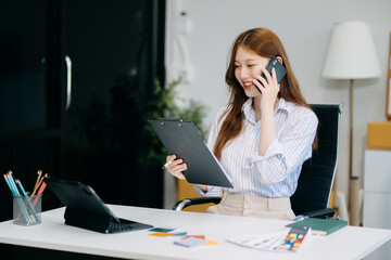 Fashion designer woman talking smart phone and using laptop with digital tablet computer in modern studio