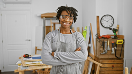 Confident woman with dreadlocks wearing safety glasses stands in a carpentry workshop