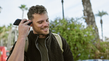 Handsome young man with a beard enjoying a voice message on a smartphone in an urban street setting.