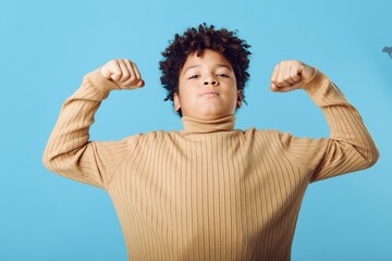 Proud african american boy flexing his muscles confidently against a bold blue background...