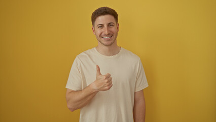Young hispanic man smiling and giving a thumbs up against an isolated yellow background in a portrait format.