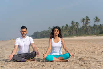 Man and woman doing yoga at the beach