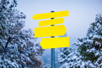 Yellow arrow boards indicating directions in a park on a blue background. Park pointers. Direction sign board. Snow-covered park in winter. Direction board.
