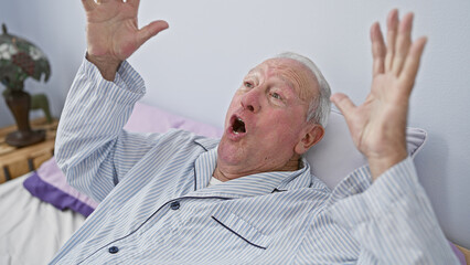 Obraz premium Confident senior man with grey hair smiling radiantly, relaxing on a comfortable bed and celebrating in his cozy bedroom.