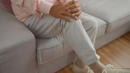 A middle-aged man sits in a cozy living room, his hands clasped on his knee, giving a sense of comfort and relaxation indoors.