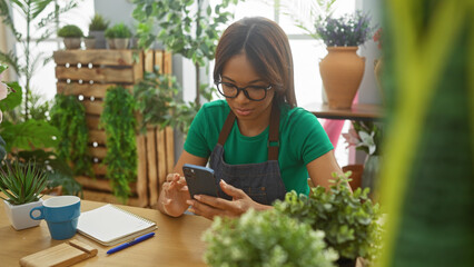 African american woman with glasses using smartphone in a green plant-filled flower shop.