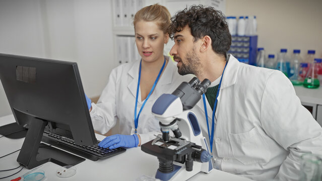 A man and woman in lab coats analyzing data on a computer in a modern laboratory setting.