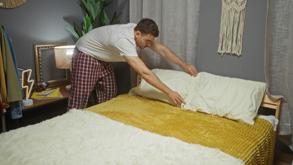 Handsome young hispanic man making a bed in a cozy bedroom, indoor setting with a modern decor and soft lighting.