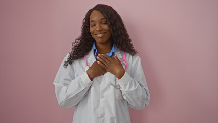 Young african american woman with curly hair and a stethoscope, smiling warmly with hands on heart...