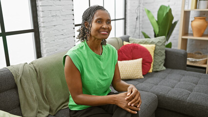 Fototapeta premium Mature african american woman sitting comfortably in a well-lit stylish living room, exuding positivity and elegance.