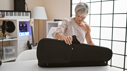 Mature woman musician unpacking her instrument in a music studio, under bright interior lights.