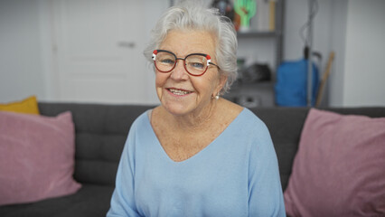 Smiling elderly woman wearing glasses sitting on a couch in a modern living room