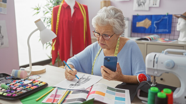 Elderly woman using smartphone in a tailor shop surrounded by sewing tools and colorful fabric swatches.