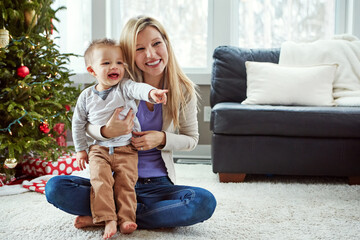 Mother, baby and happy christmas while on floor in living room, holiday and bonding for love. Motherhood, parent and toddler with woman together, hug and play with sitting or pointing at home