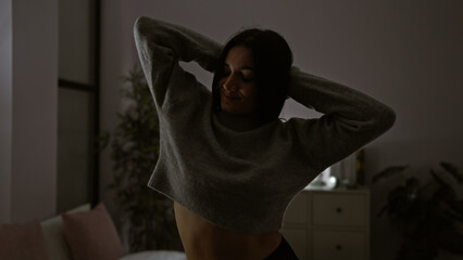 A serene young hispanic woman enjoys a peaceful moment alone in a dimly lit bedroom at night.